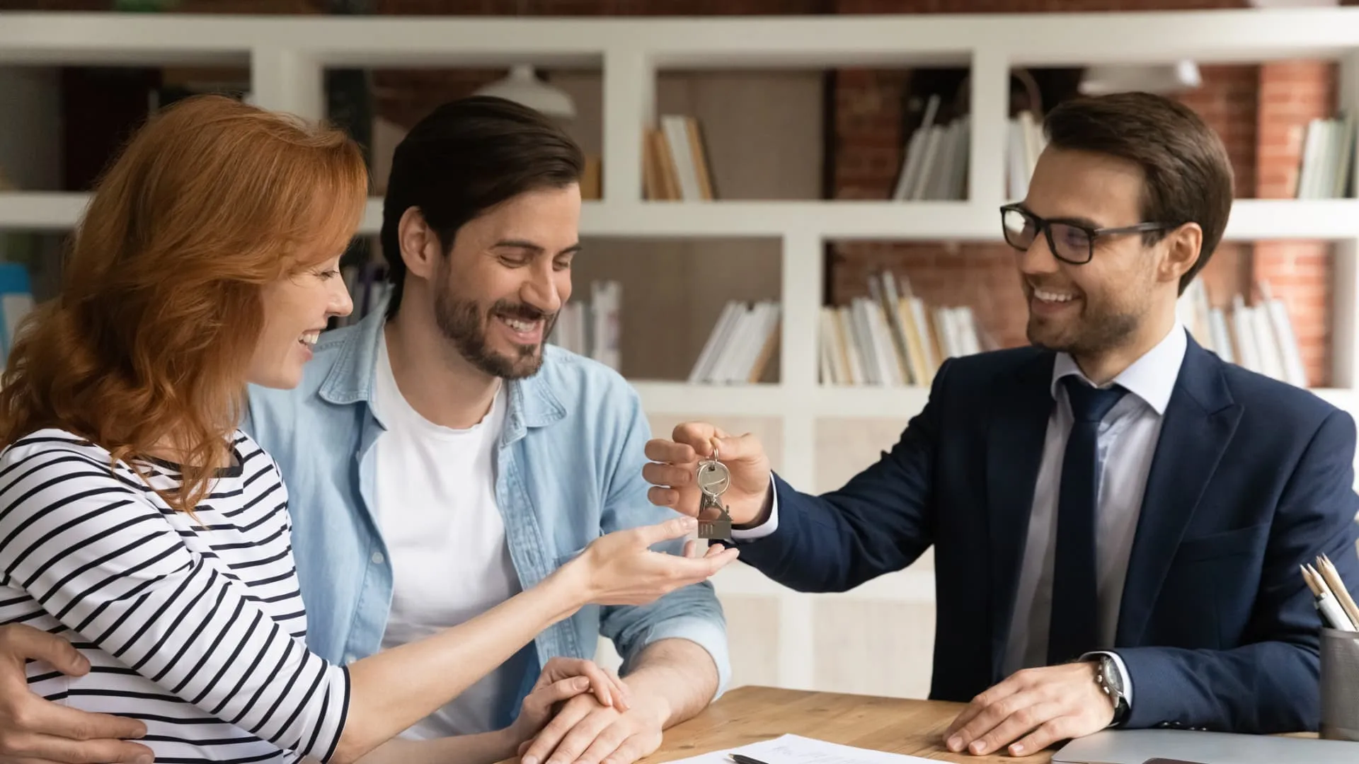 Real estate broker handing house key to a smiling young couple