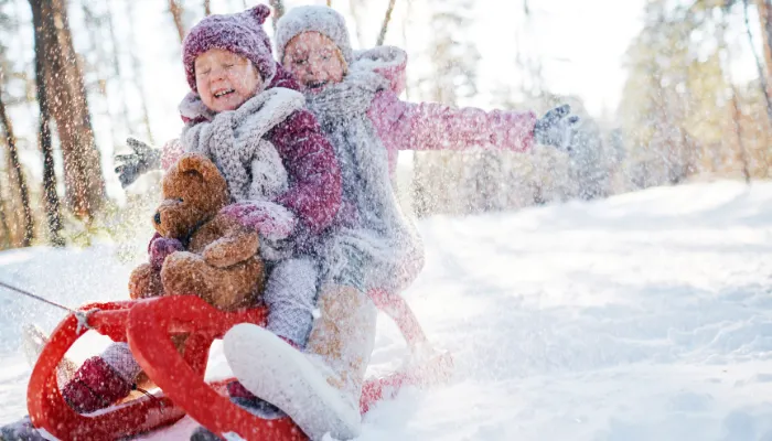 Two kids sledding and having fun in the snow.