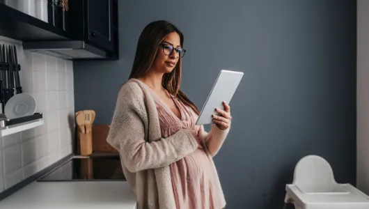 Image of a pregnant woman holding her belly and reading her tablet 