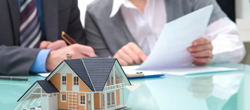 Miniature house at the table while real estate brokers are discussing documents.