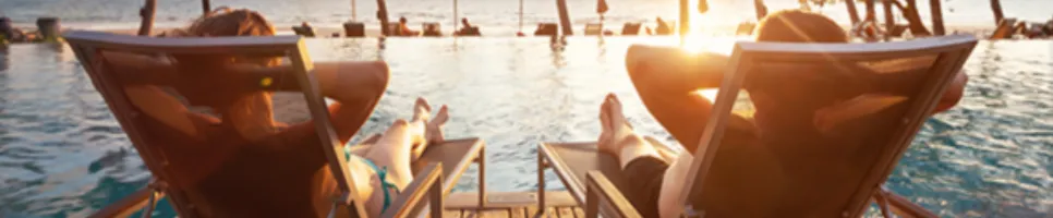 two people in beach chairs staring at the sunset over the water