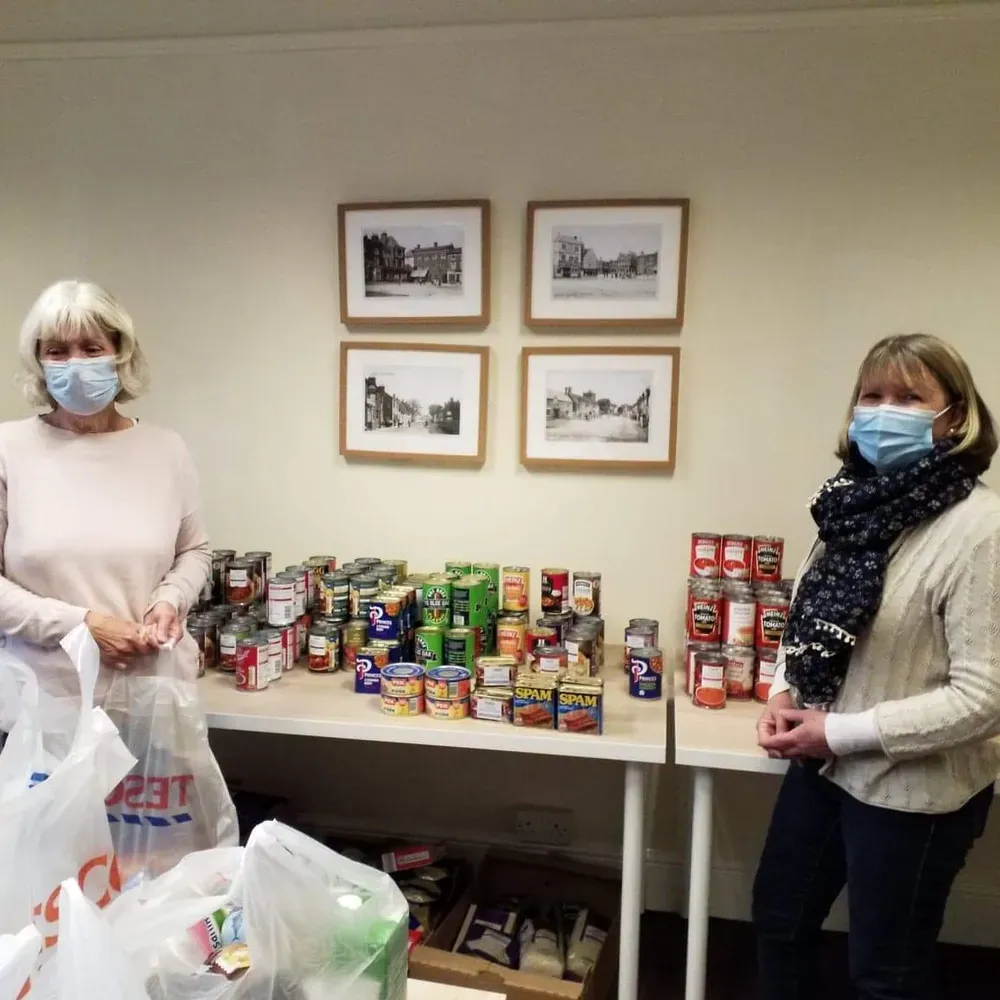 Two Food Cupboard volunteers wear masks as they pack shopping bags