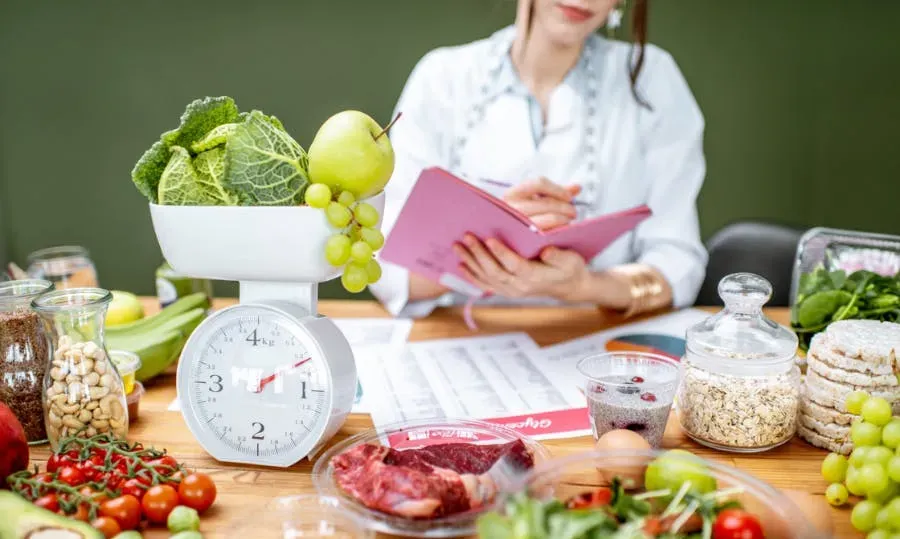 image of a woman with a notebook surrounded by food with some being weighed