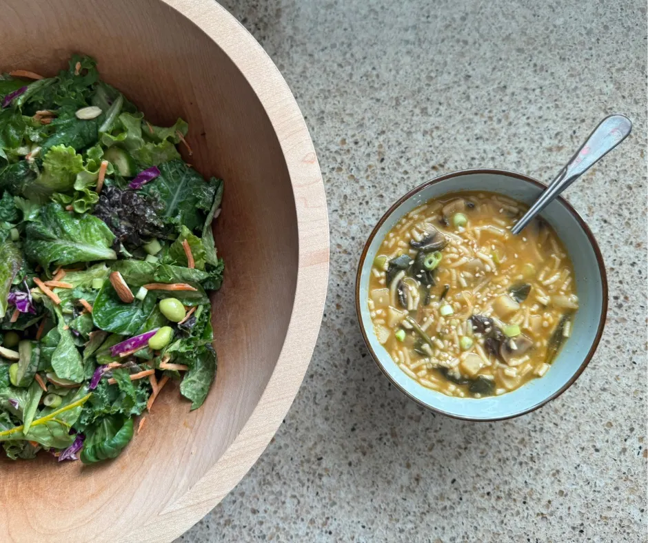 Large leafy green salad with vegetables served alongside a warm vegetable soup as a complete plant-based meal