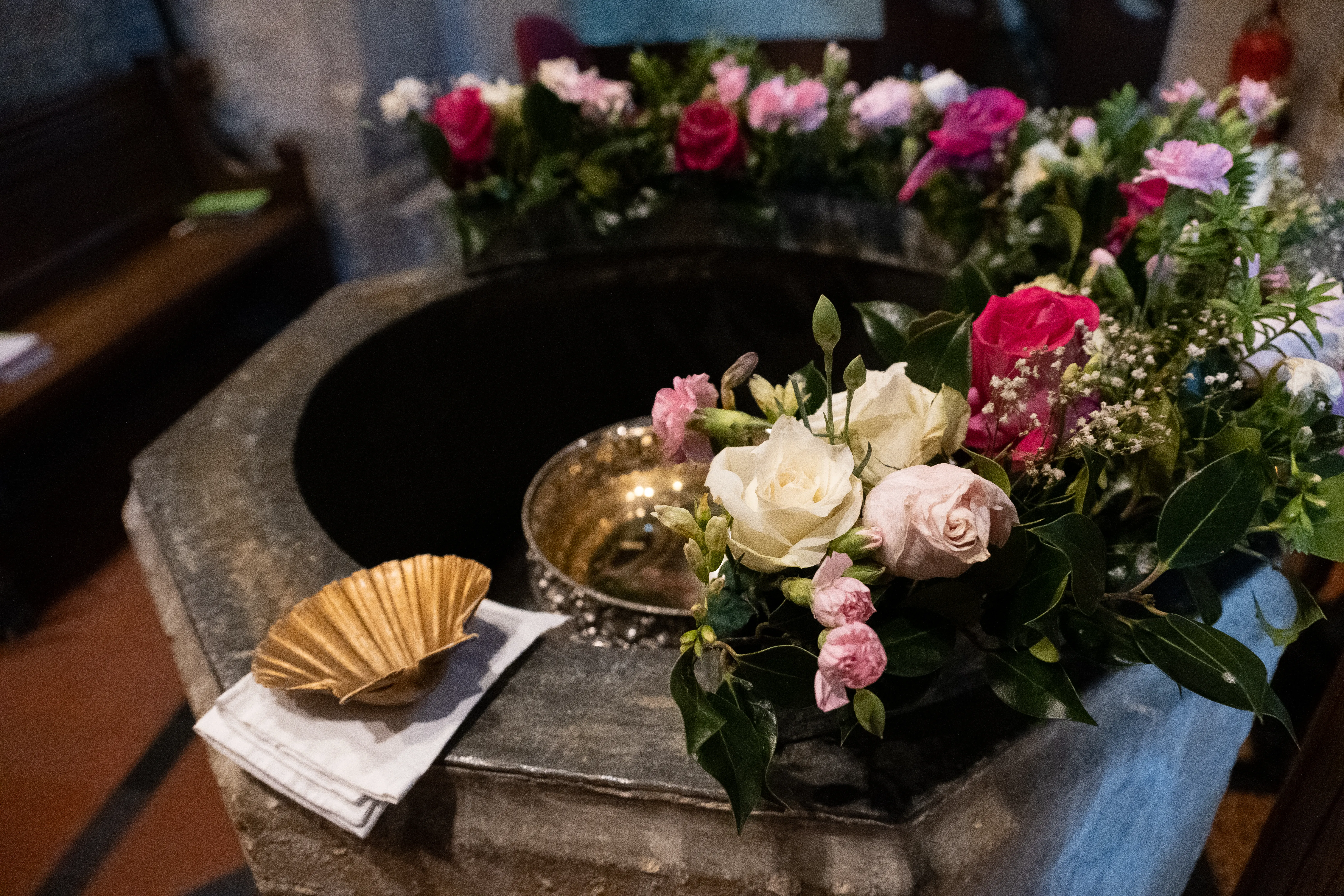 The St Laurence font decorated in pink and white roses, with a small gold seashell on the side, ready for a baptism