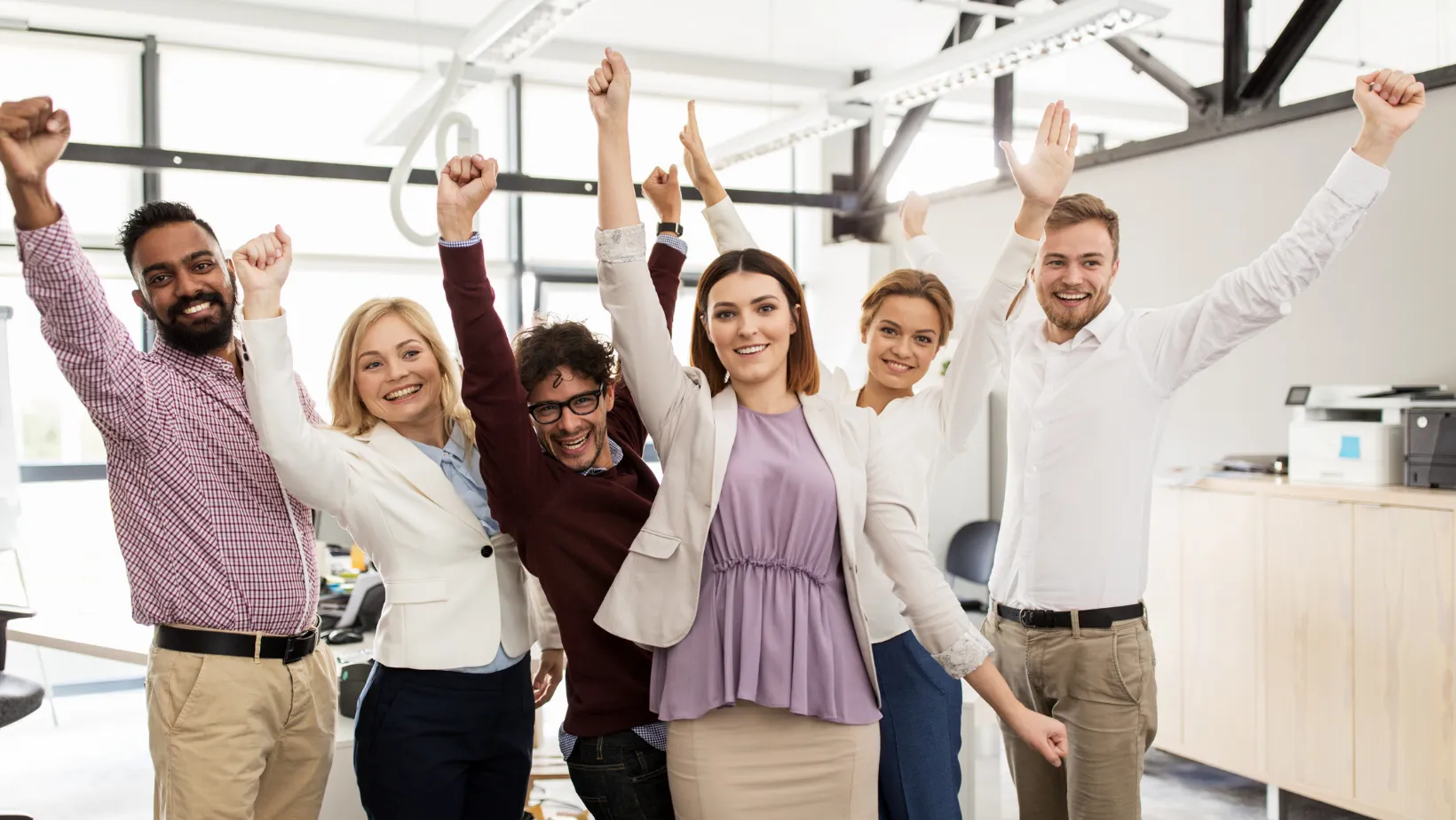 A stock image of a team of men and women in an office space, smiling and with their hands raised in the air. 