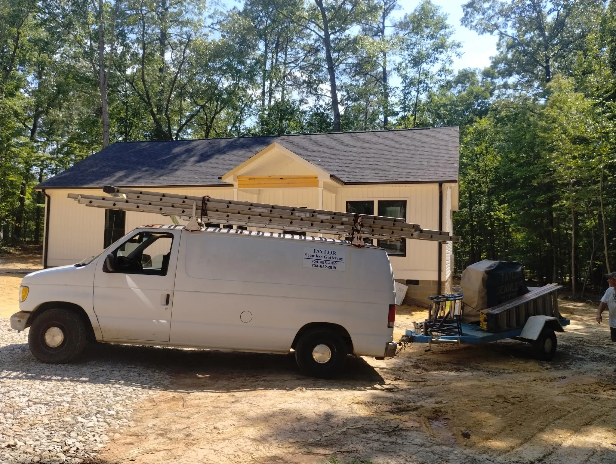 Taylor's Seamless Guttering work van and custom fabrication trailer on-site for a residential gutter installation.