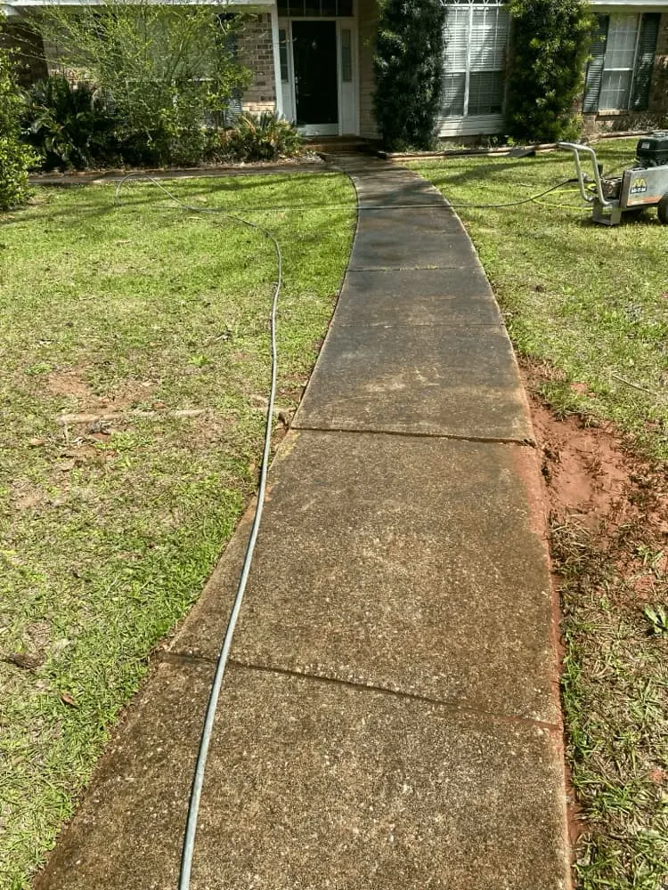 <alt=“Before concrete sidewalk pressure washing in Mobile County, Alabama showing heavy dirt and discoloration on curved walkway.”>
