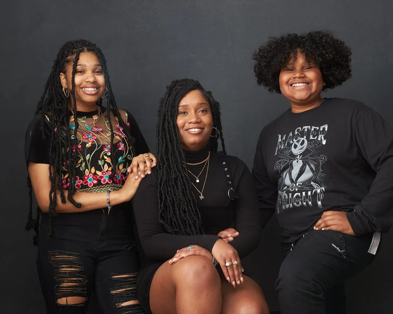 Family portrait of three children all wearing black posed in front of a dark grey backdrop