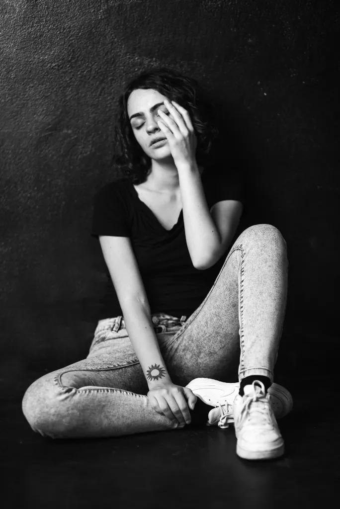 ritratto di giovane donna con jeans e t-shirt, seduta per terra, mano sul viso, capelli neri, fotografia professionale in bianco e nero, studio fotografico a Milano, Federica Nardese fotografa per book fotografici e ricordi stampati, ritratti d'autore