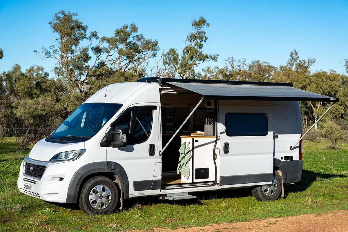 White Fiat Ducato campervan with awning extended in the Australian bush, showing exterior layout of Matthew Storer’s self-built van