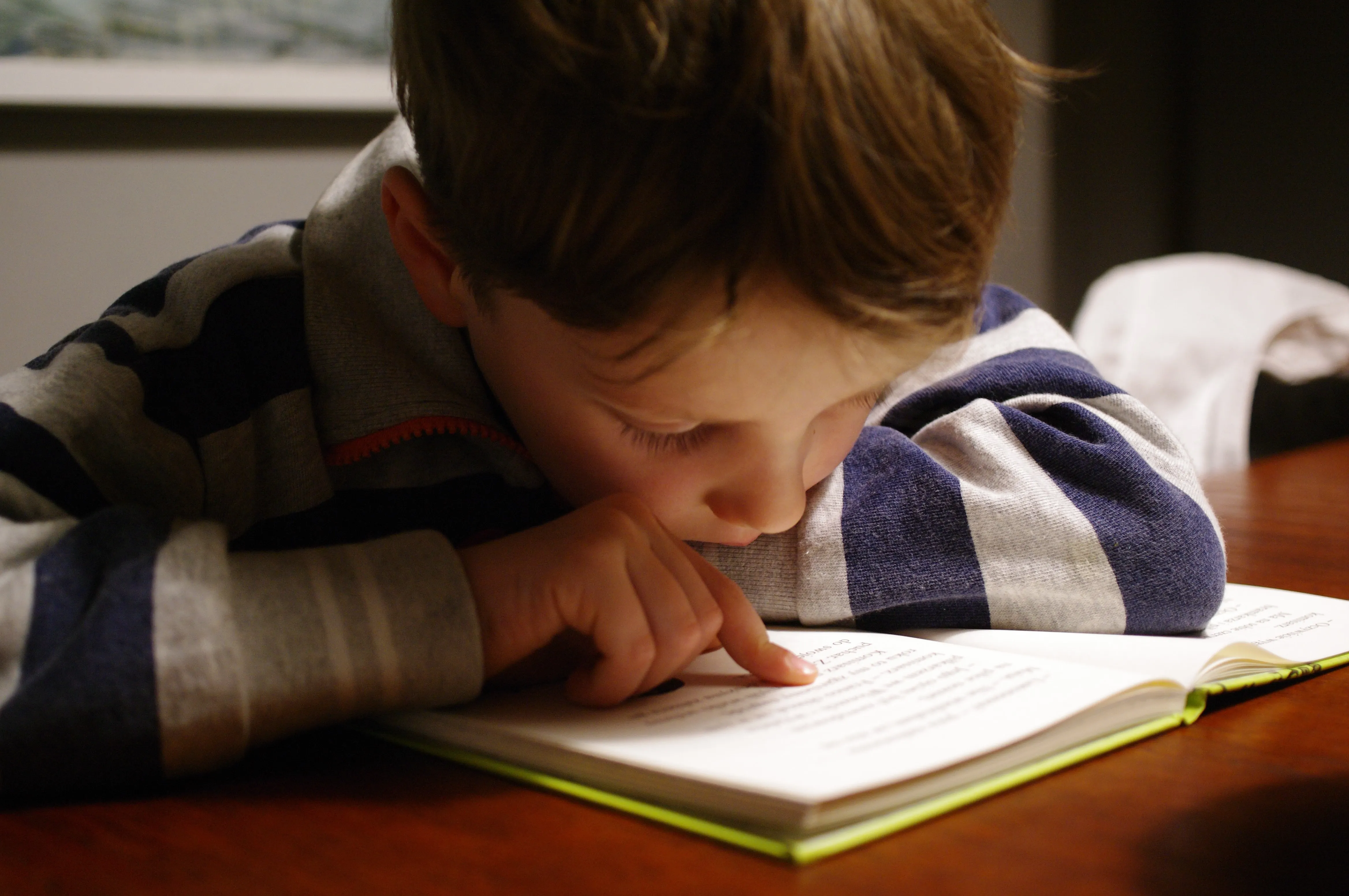 child reading a book with one finger on text