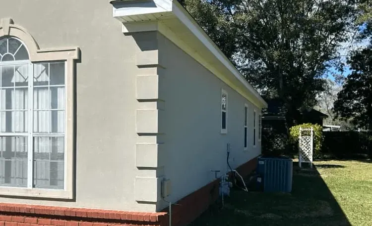 <alt=“After stucco house soft wash in Dawes, Mobile County, Alabama showing clean exterior walls bright trim and restored brick foundation.”>