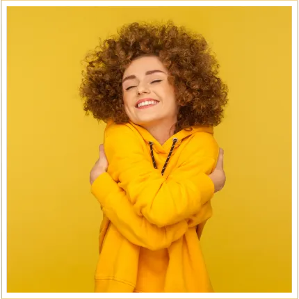 Smiling woman hugging herself wearing a bright yellow sweater