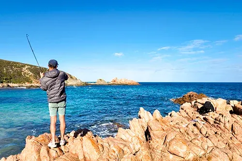 Rock fishing from coastal headland using spinning rod in clear blue water