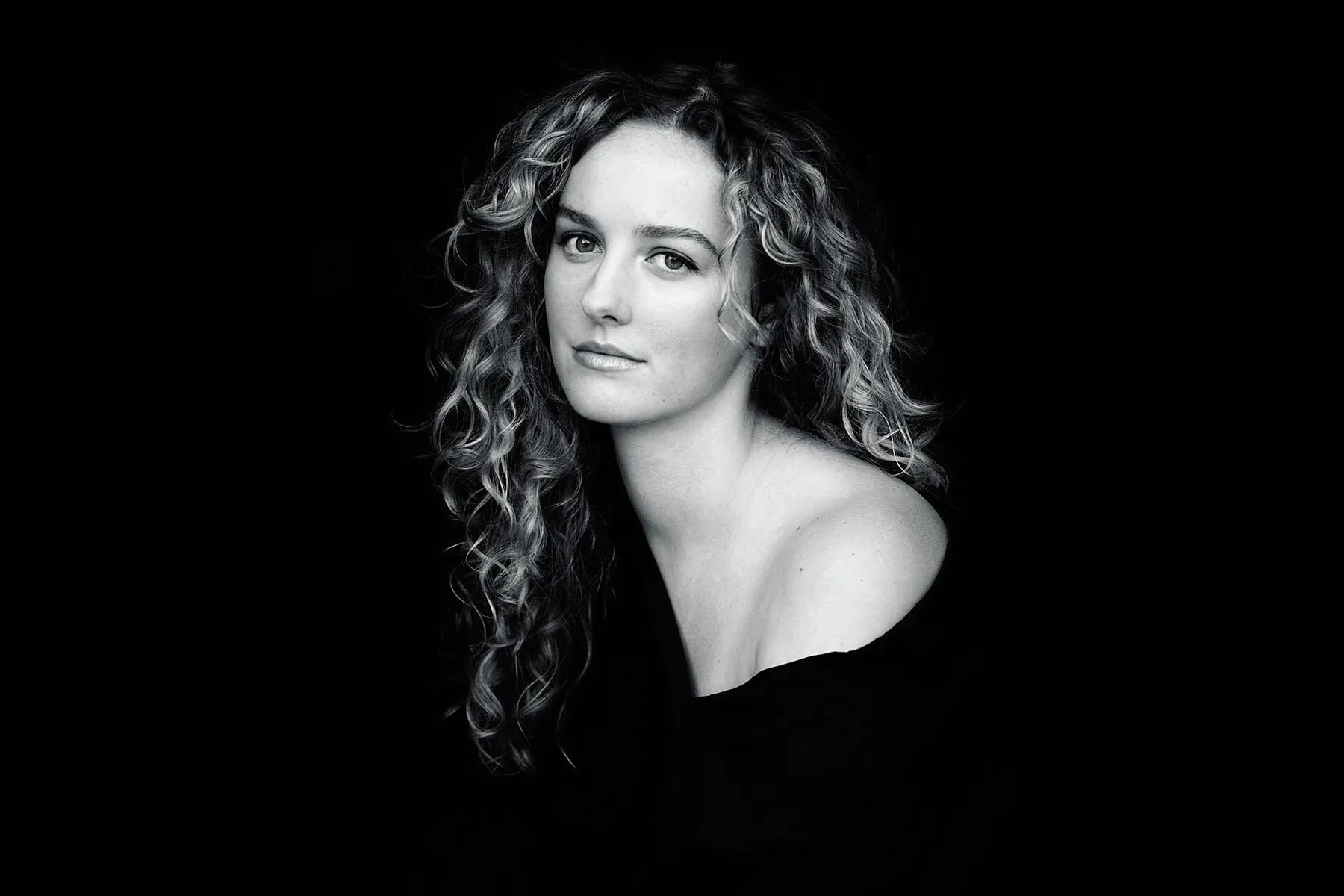 Dark portrait of woman with curly hair wearing a black off the shoulder sweater