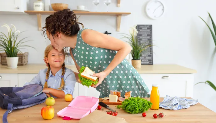 Mom kissing her daughter's forehead while packing her school lunch.