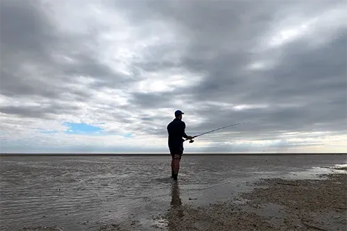 Man wading in shallow water fishing with soft plastics under dramatic sky