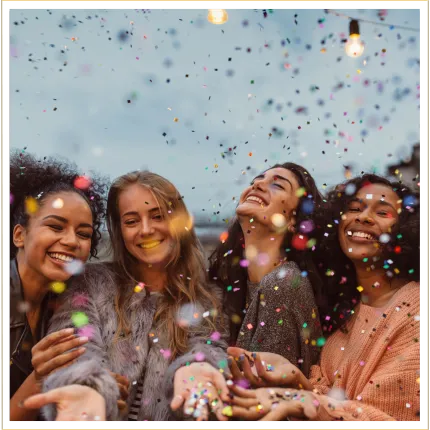 Four women celebrating together smiling with confetti in the air