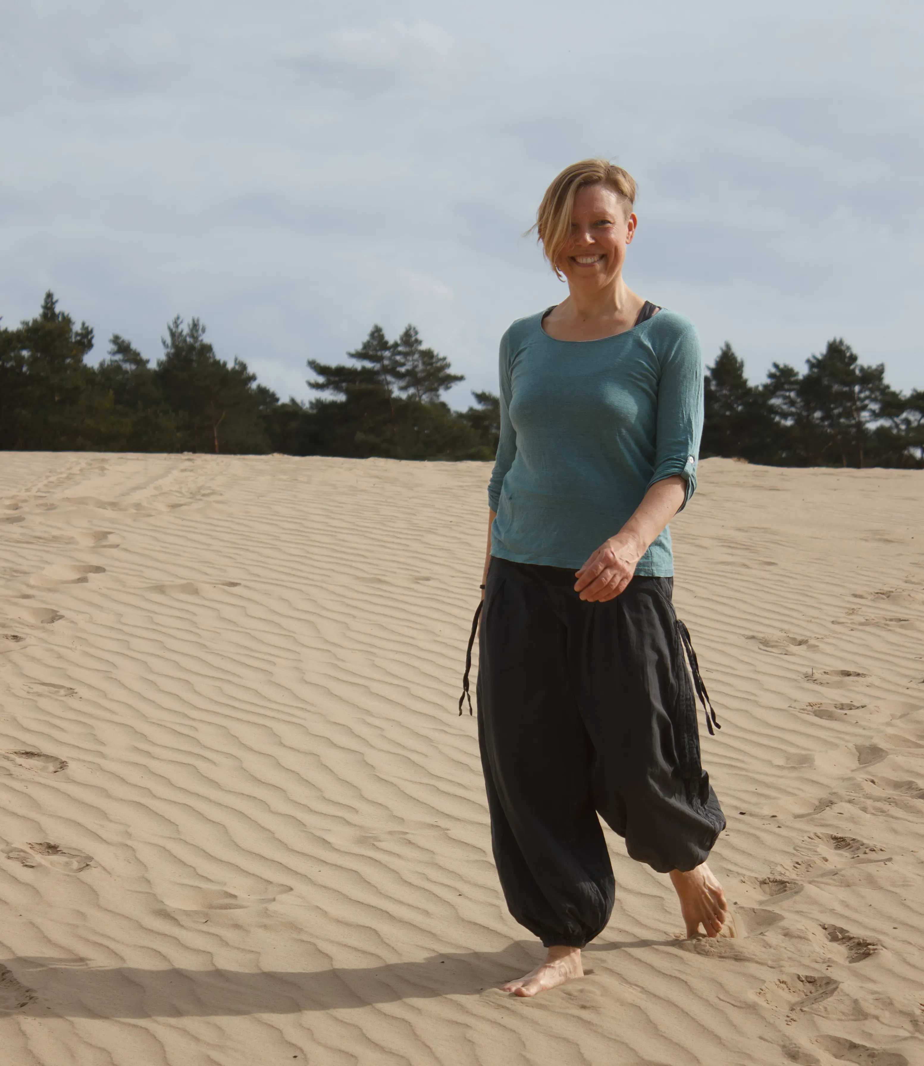Ingrid loopt op het zand en kijkt lachend in de camera