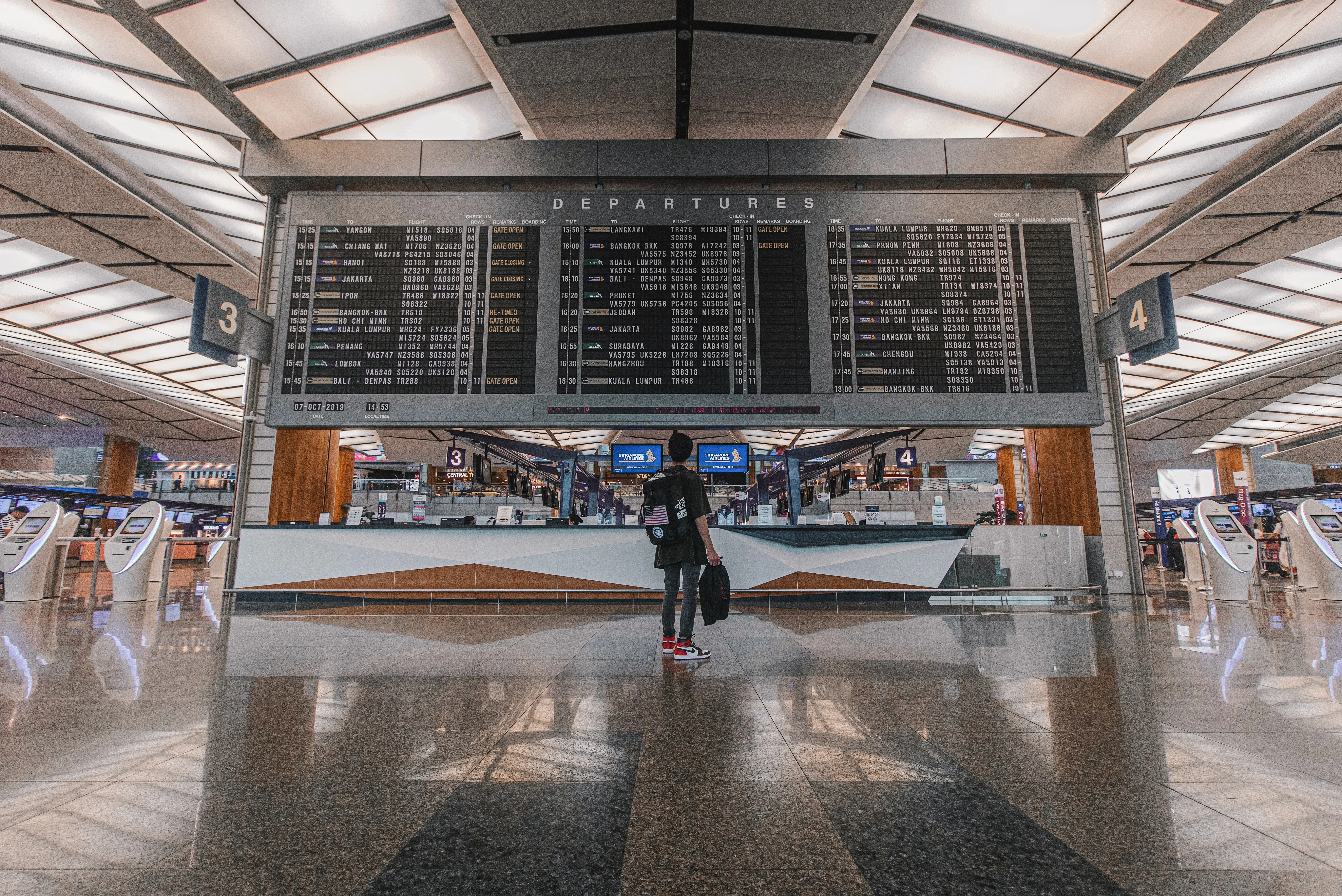 young person standing in airport terminal alone looking at the board with flight details