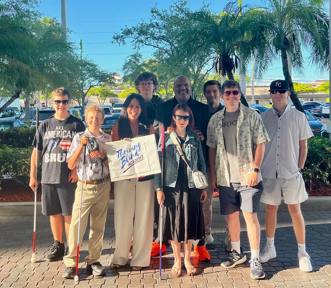 a group of young people many holding white canes and one person holding a thriving blind acacemy sign