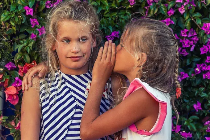 little girl whispering to another girl