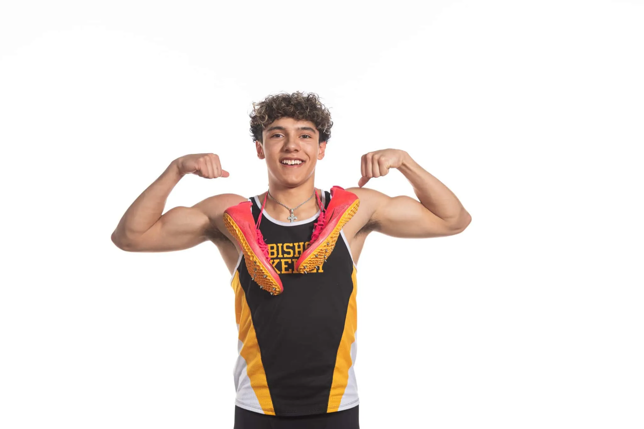 Bishop Kelly High School senior smiling and flexing for the camera with track spiked shoes around his neck.