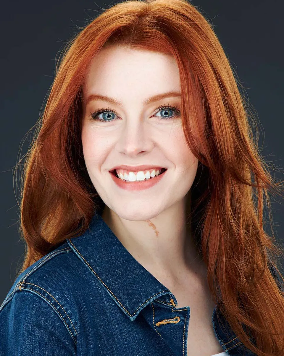 Vibrant acting headshot of red haired woman smiling wearing a jean jacket