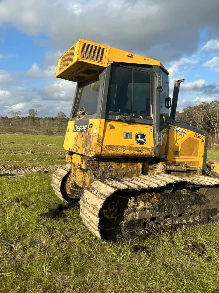 <alt=“Before heavy equipment pressure washing in Hurley, Jackson County, Mississippi showing mud-covered John Deere bulldozer with buildup on tracks and body.”>
