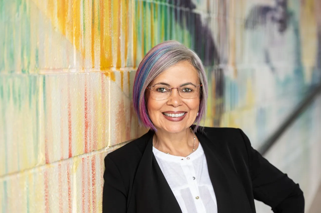 Picture of Cora Bracho-Troconis standing in front of a colorful painted wall