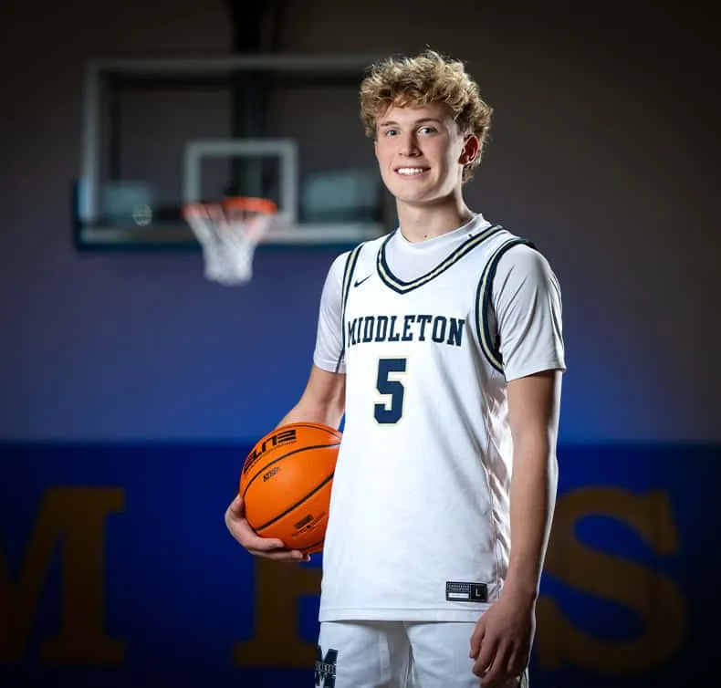 Middleton basketball player wearing number 5 white jersey posing with basketball in gym, team photo portrait with basketball hoop in background