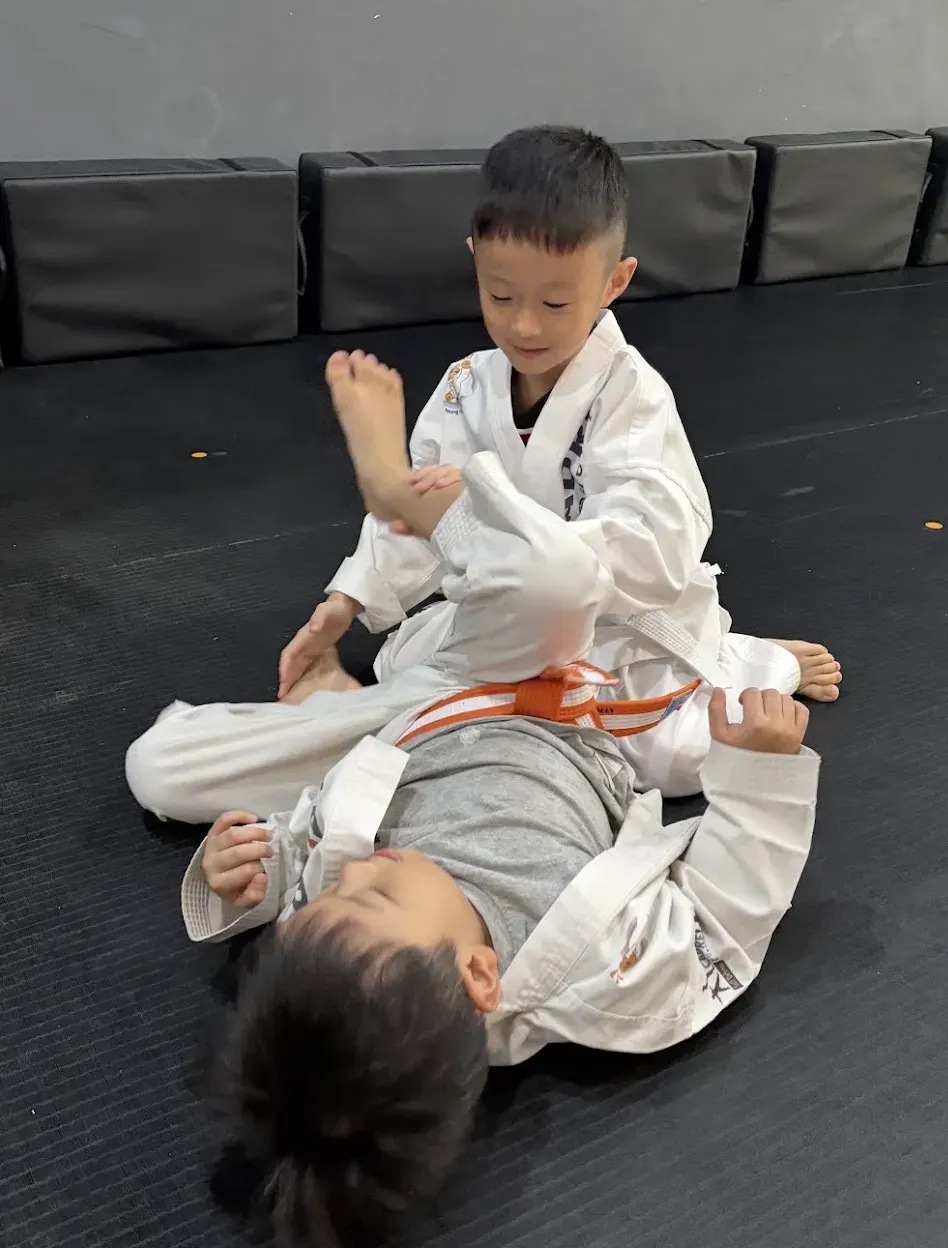 Two children practising grappling and positional control during a Kids Integrated Jiujitsu class at CADRE Academy in Singapore.