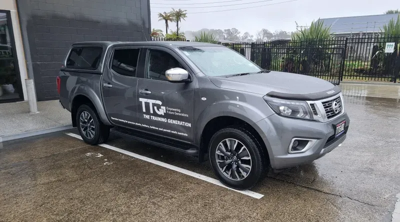 A grey Nissan Navara pickup truck with company branding from 