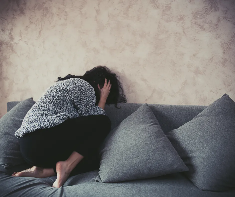 trauma-informed coaching; woman in fetal position against harassment at home; abused; abuse; adult,; against aggression; unarmed young woman at home; fetal position on sofa protecting herself from violence and sexual harassment