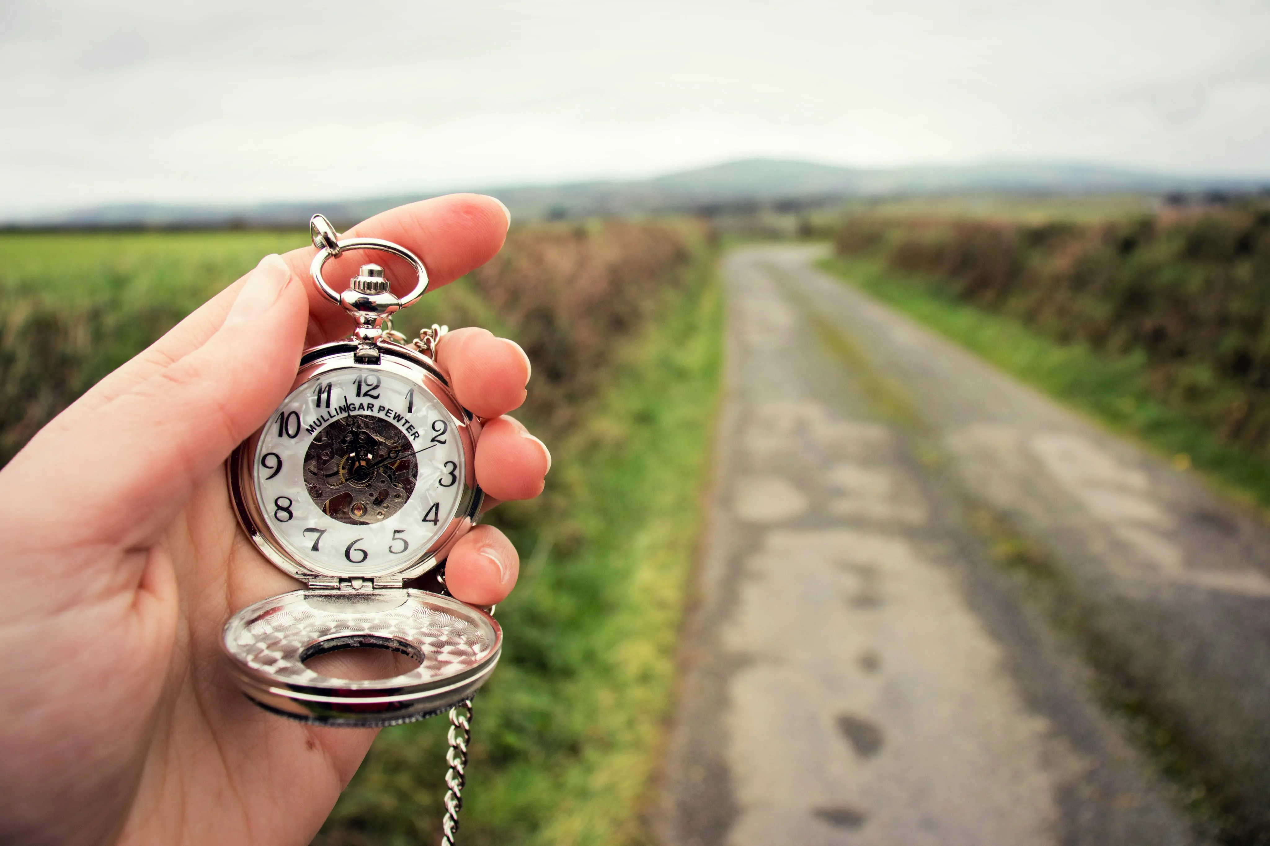 Hand holding pocket watch next to a long road