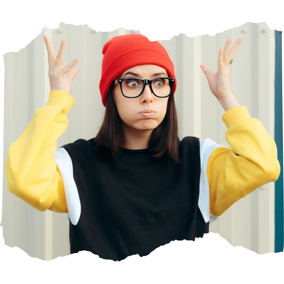 Person in a red hat and black glasses wearing a black t-shirt with a long sleeved yellow shirt underneath holds their hands up by their head making a mind-blown gesture