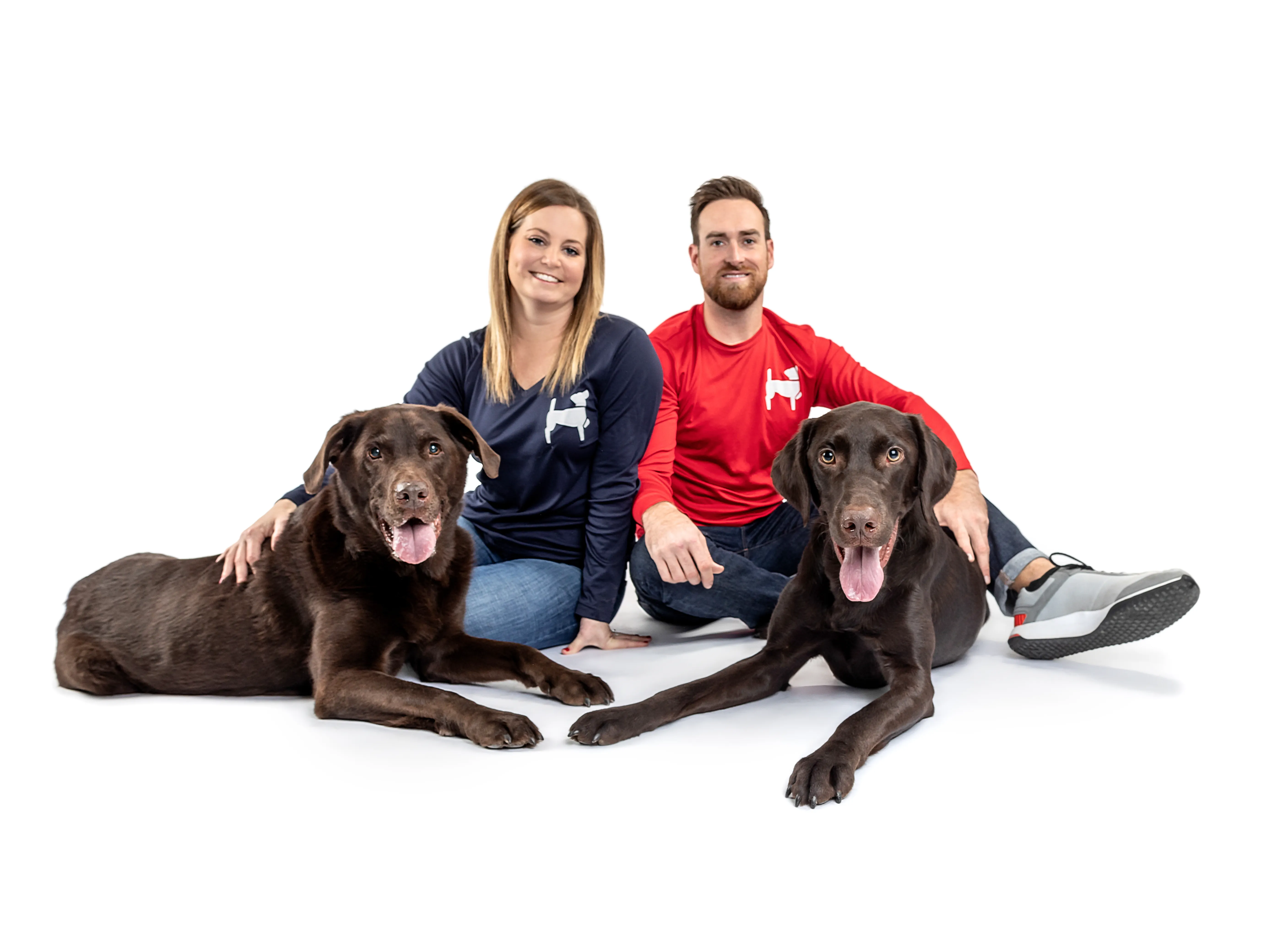 Professional dog trainers Jena and Derek from Newman's Dog Training sitting with two chocolate Labrador retrievers — experts in in-home dog training, basic obedience, leash reactivity, and service dog preparation in Northwest Arkansas and Kansas City.