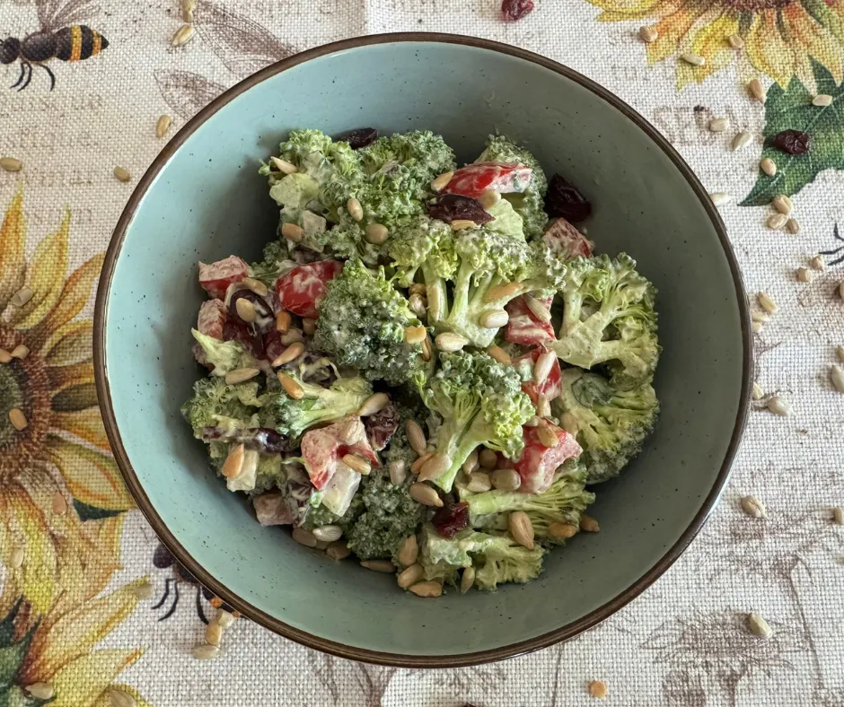 Creamy plant-based broccoli salad with red bell pepper, red onion, parsley, dried cranberries, and sunflower seeds.