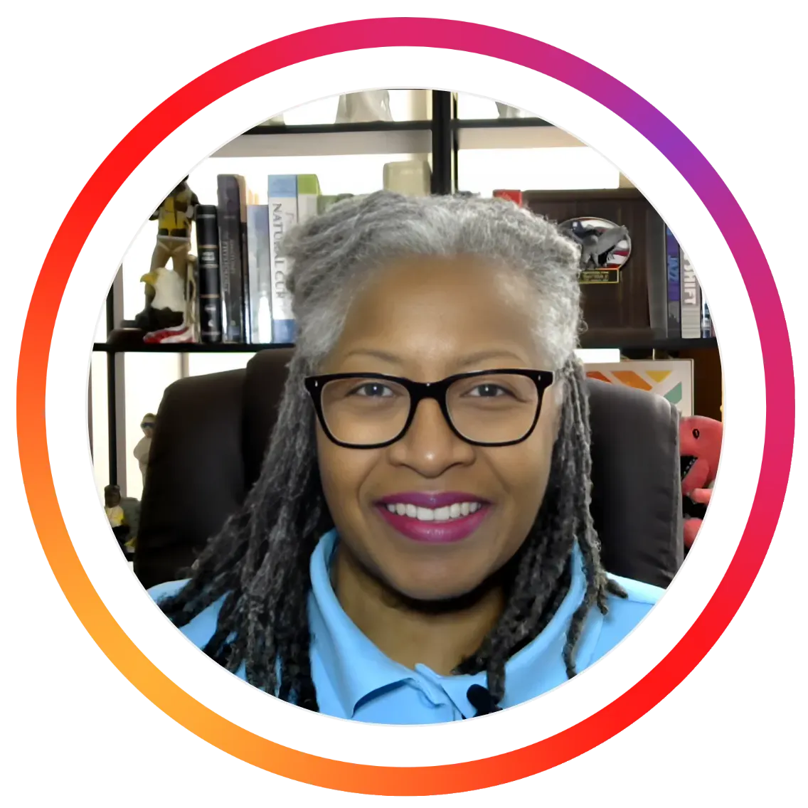 Professional profile photo of Dr. Lisa Singletary, MD, MPH, CWHC, smiling while seated in her office. She wears black-framed glasses and a light blue collared shirt, with silver-gray locs styled neatly around her shoulders. Bookshelves and office décor are visible in the background. The image is framed within a circular border featuring a vibrant pink, orange, and purple gradient, making it ideal for wellness coaching, health education, speaker profiles, webinars, and social media branding.