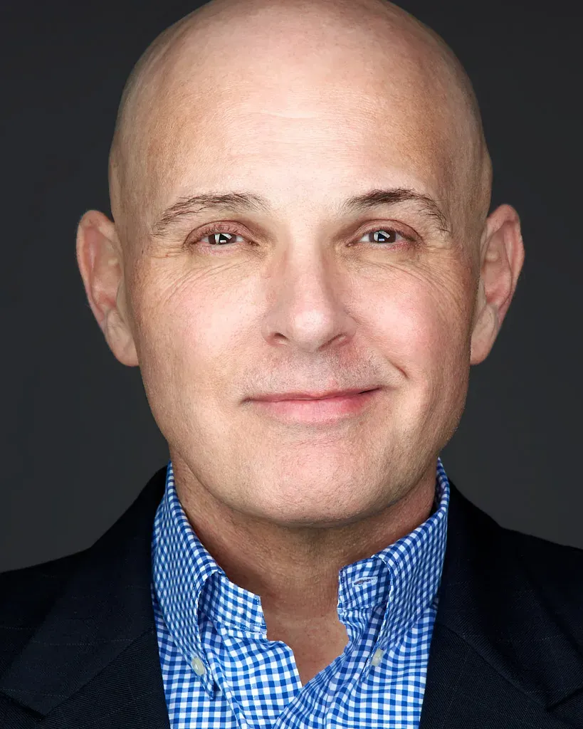 Professional headshot of bald man in a suit smiling in front of a white backdrop