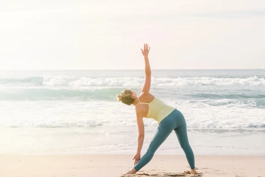 A woman on a yoga pose standing on a shore facing the ocean.