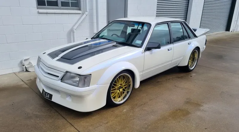 A white, classic Holden VK Commodore sedan with gold wheels, freshly detailed and parked in Rotorua, demonstrating HGD Detailing's expertise in classic car care.