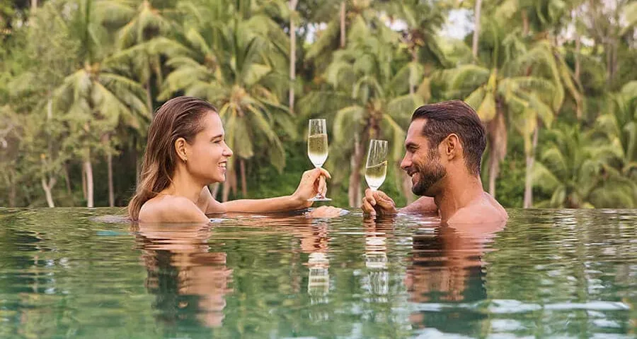 a couple doing a champagne toast in an infinite pool in the tropics.
