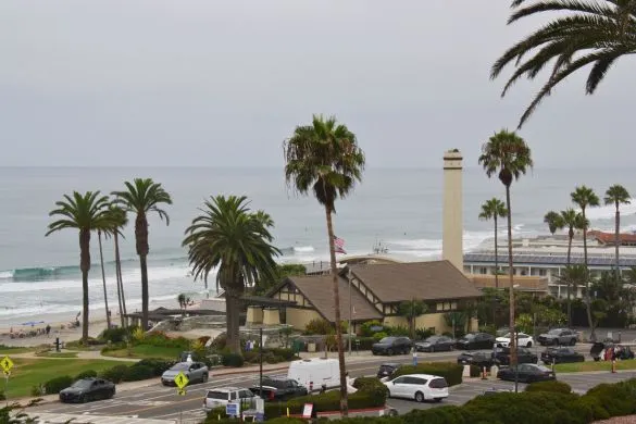 View of Powerhouse Park in Del Mar, with park, palm trees, beachgoers and the ocean in the background.