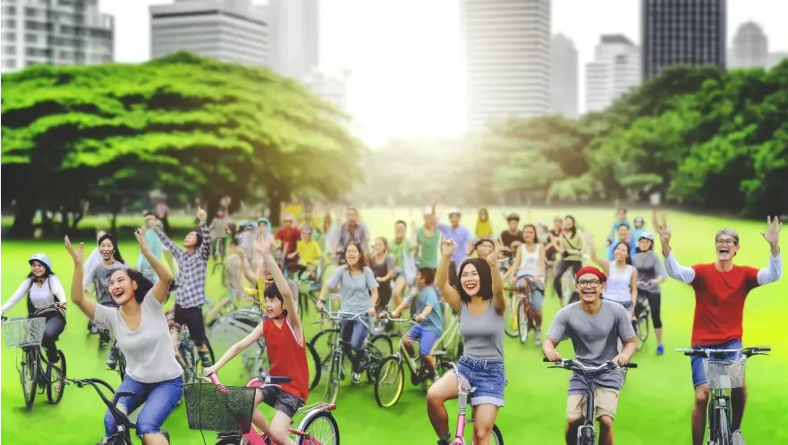 A racially diverse group riding bicycles in the park smiling and waving.