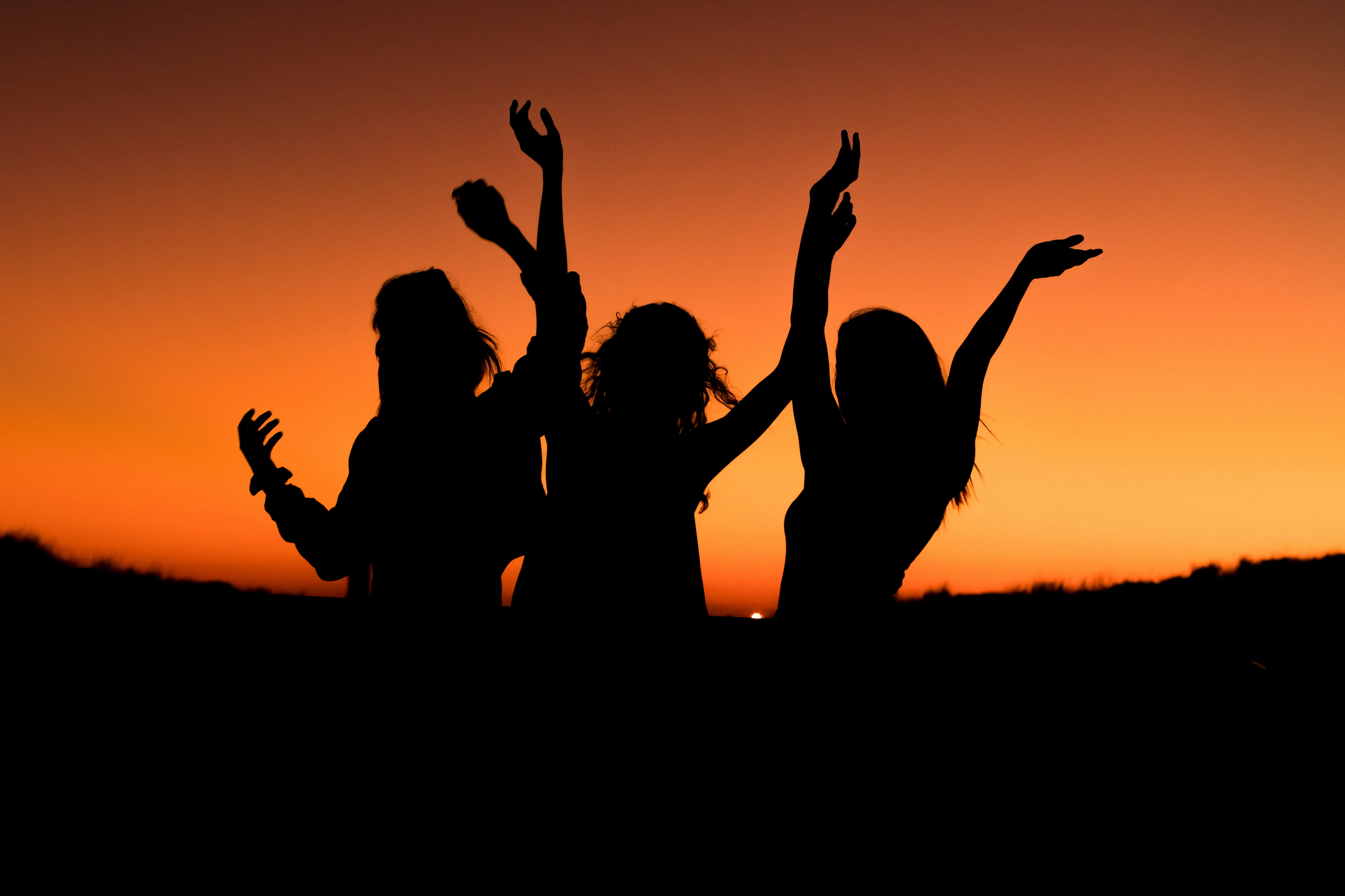 A shadow image of 3 women with their hands raised in the sky