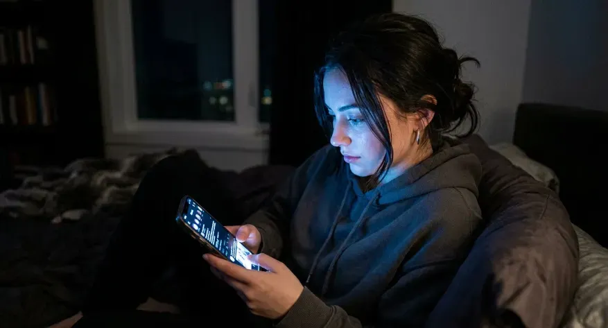 Person using a smartphone at night with blue light illuminating the face