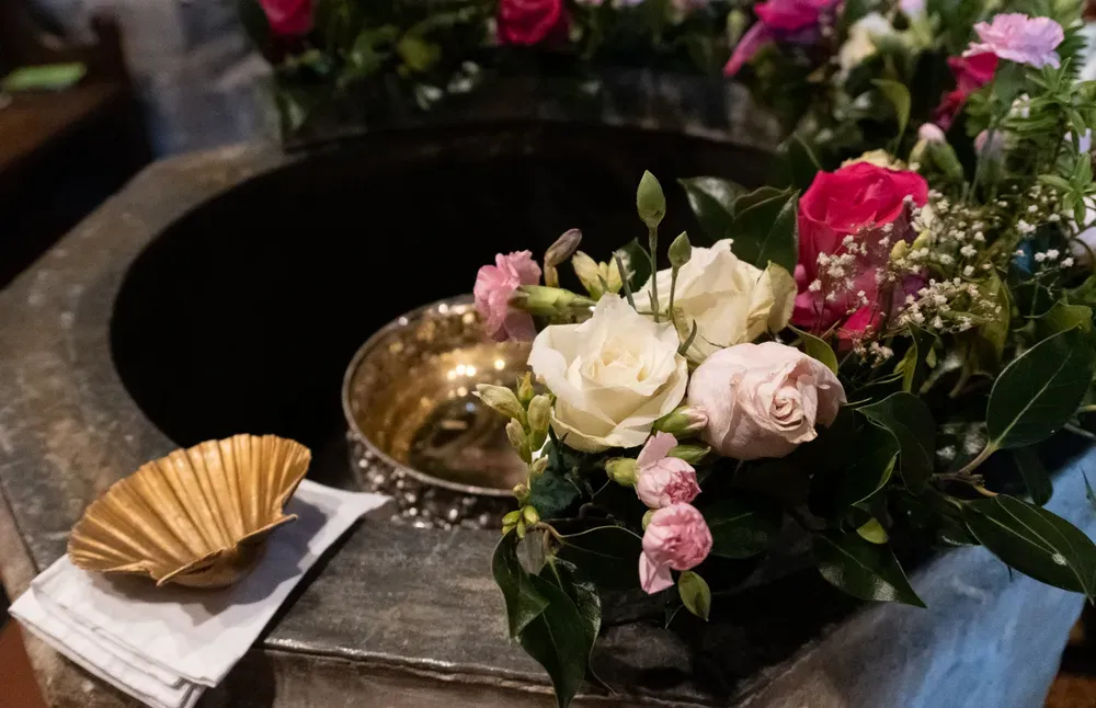 The St Laurence font decorated in pink and white roses, with a small gold seashell on the side, ready for a baptism