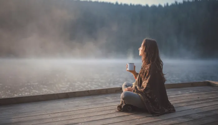 A woman enjoying a cup of coffee on a dock at a lake.